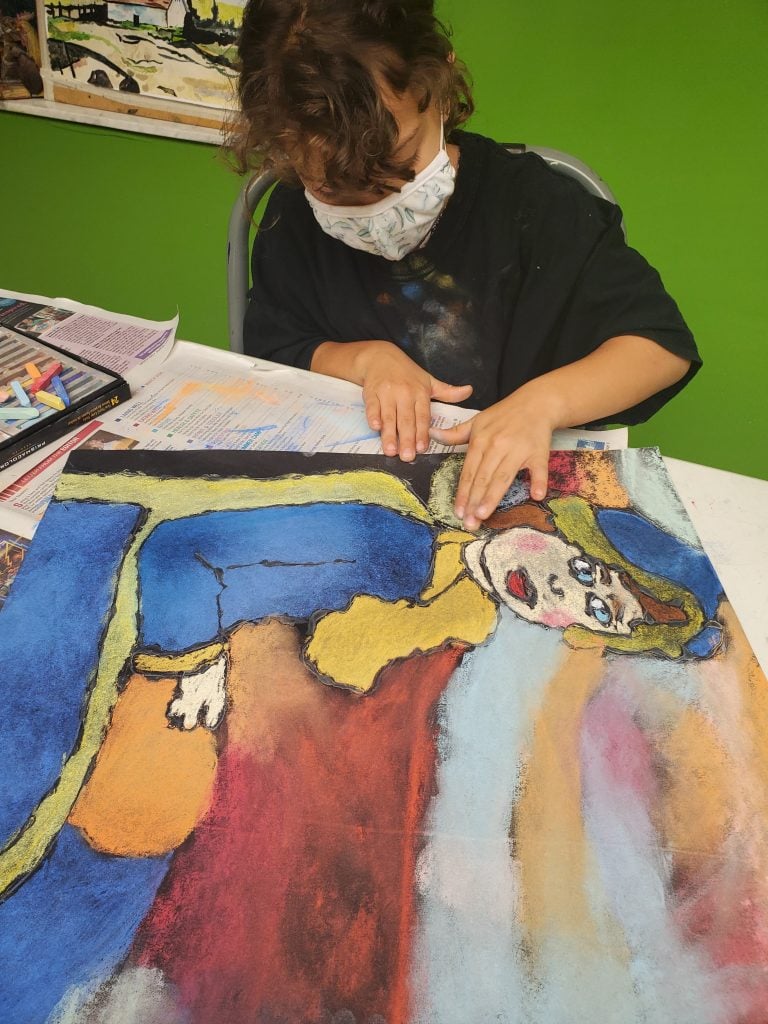 Young girl drawing a colorful charcoal picture of a woman wearing yellow and blue sitting in a chair