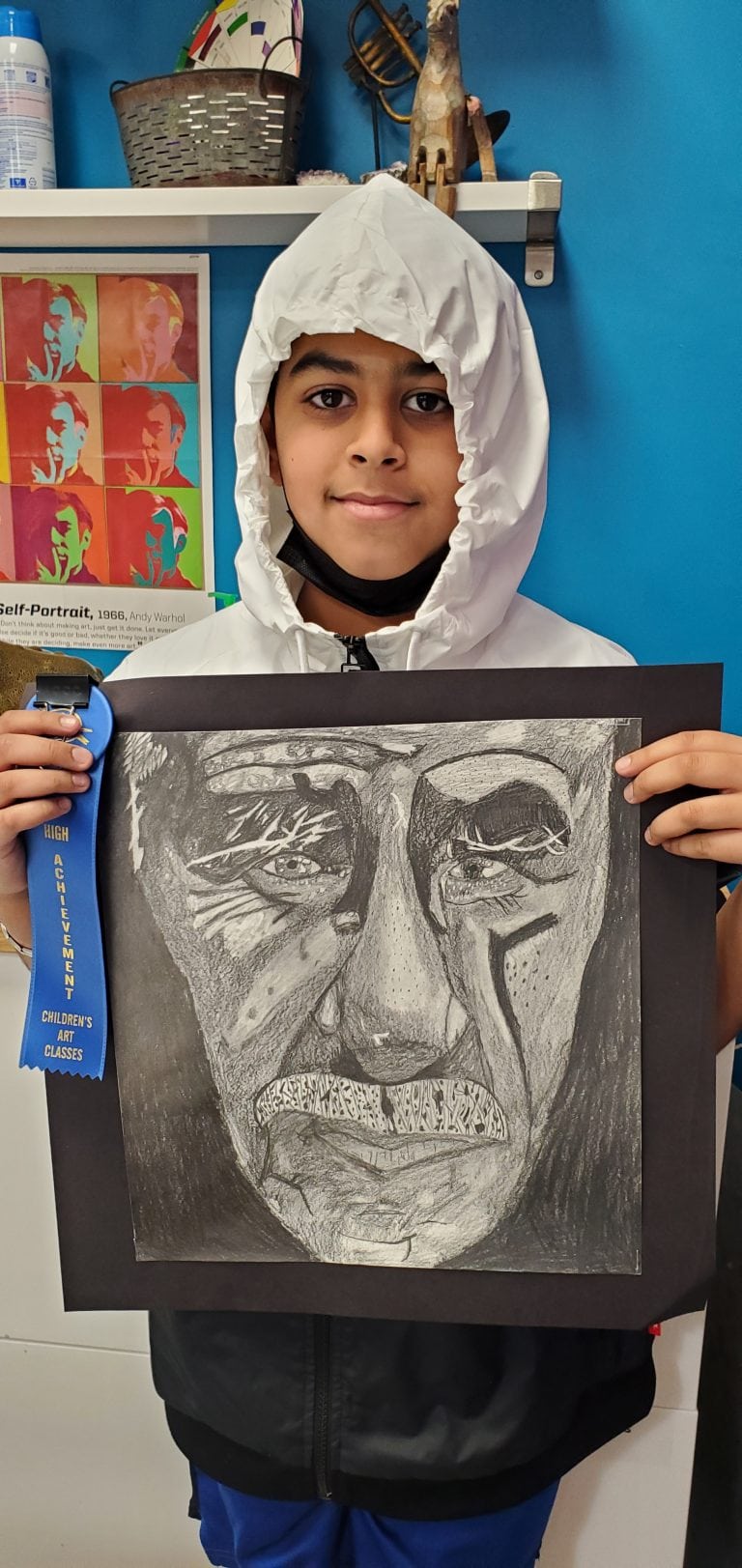 Young boy holding charcoal drawing portrait with a blue ribbon award
