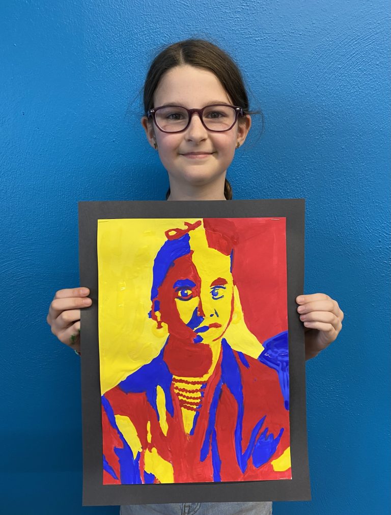 Young girl wearing glasses holding a red, yellow and blue portrait of a woman painting