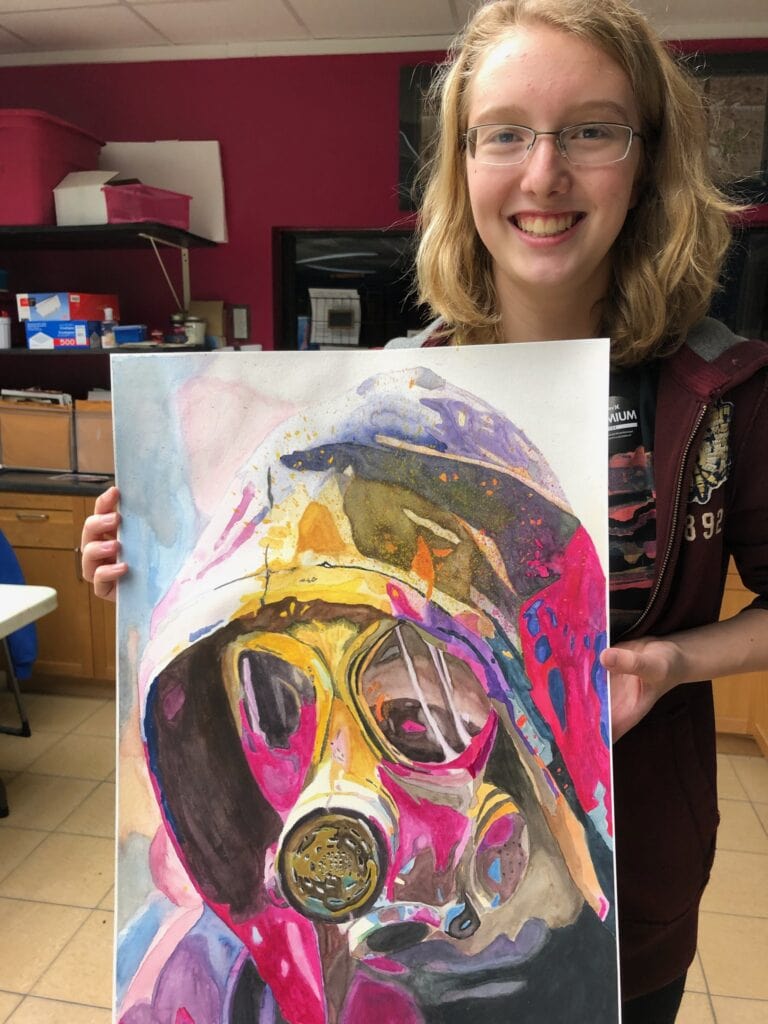 Blonde girl with glasses holding a colorful painting of a person in a gas mask and wearing a hooded coat